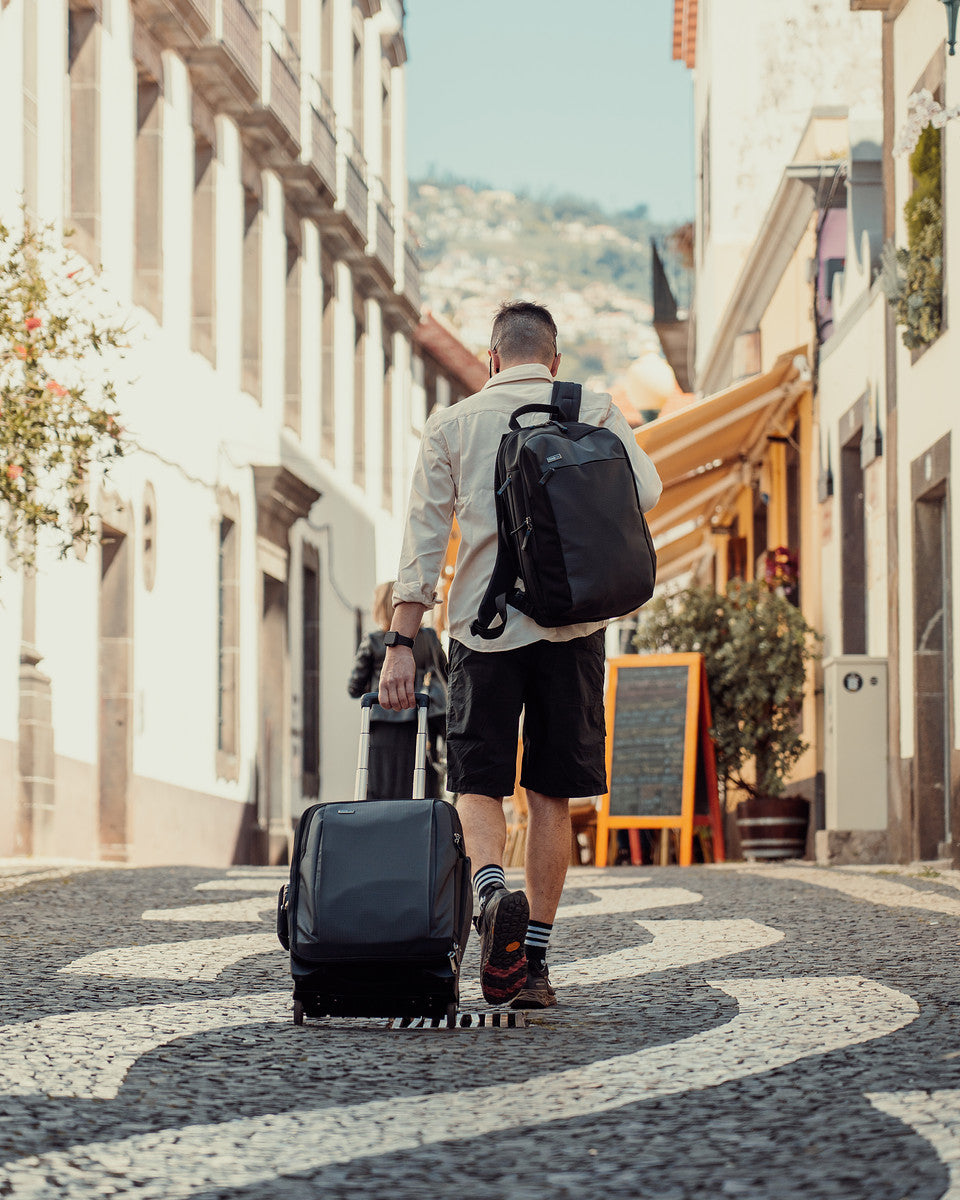 Person walking with rolling travel bag and backpack from Think Tank