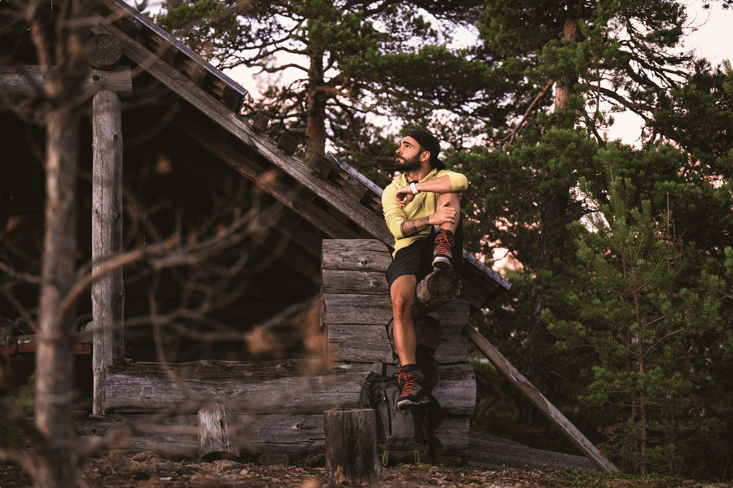a man sitting on a cabin holding his leg, gazing into the forest