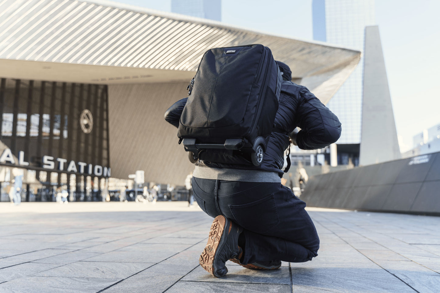 A man crouching down, view from the backside, wearing a roller backpack