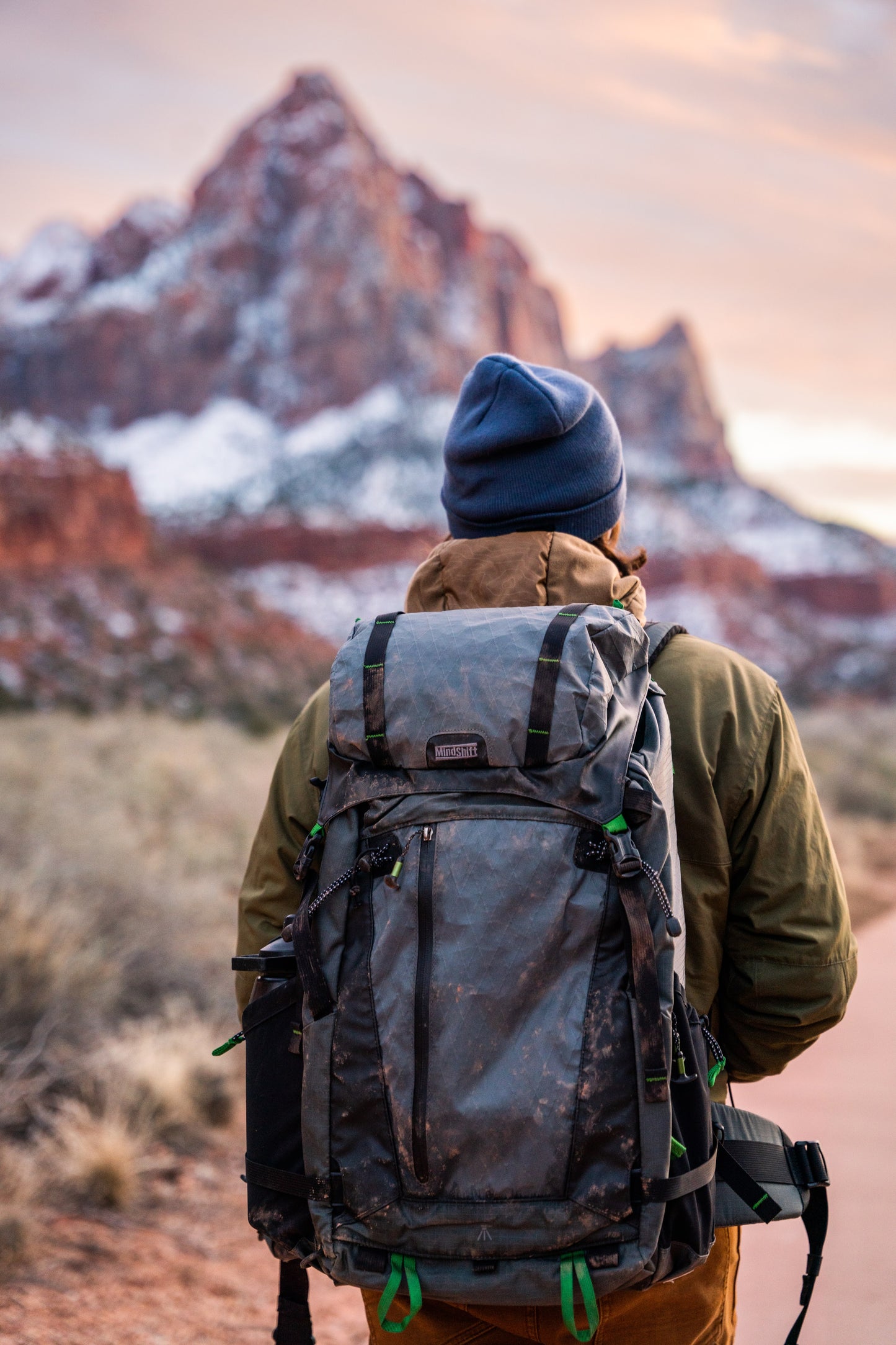 A man wearing a backpack, and a out of focus view of a mountain in the distance 