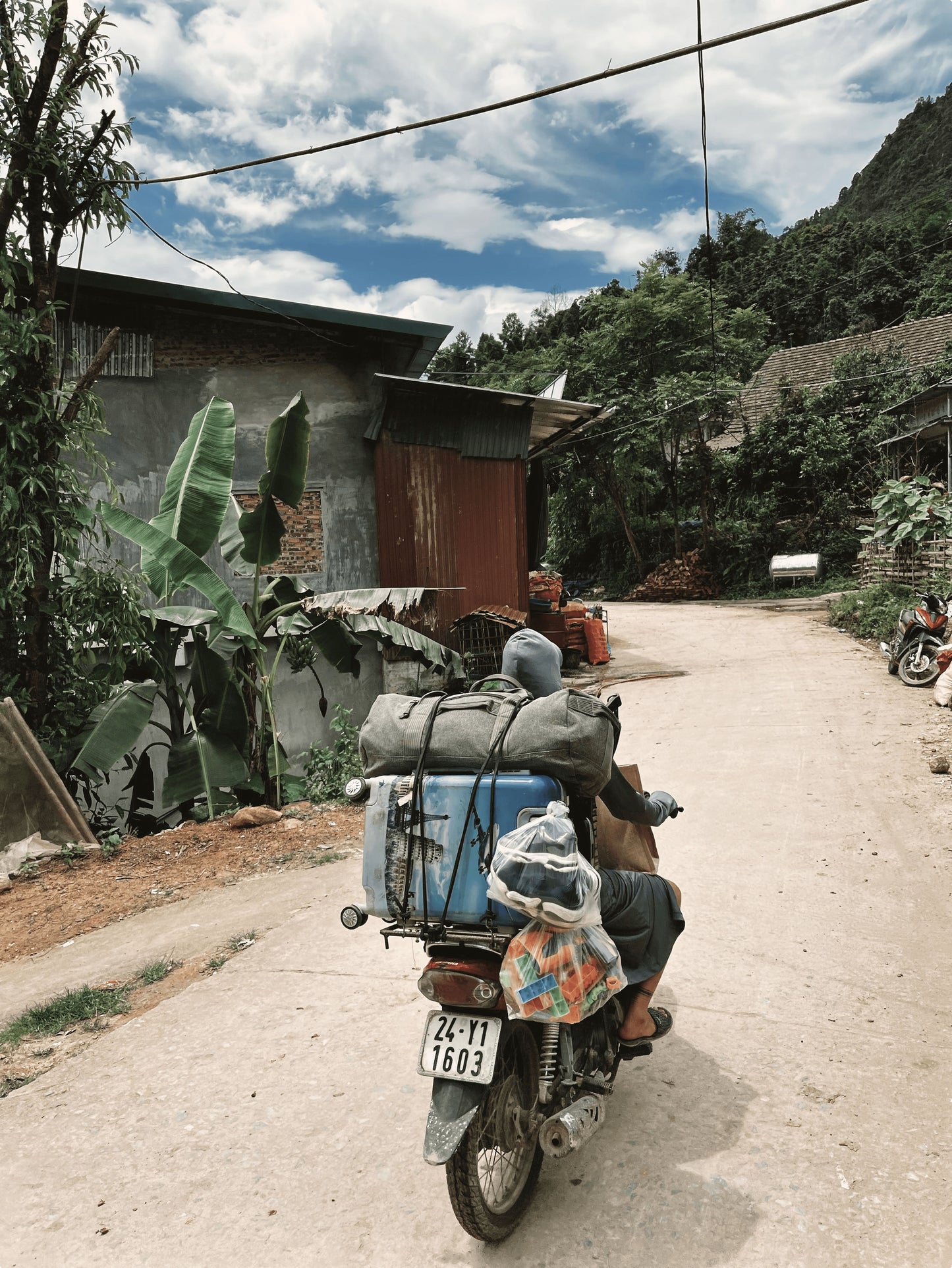 A person riding a moped, with several luggage strapped in