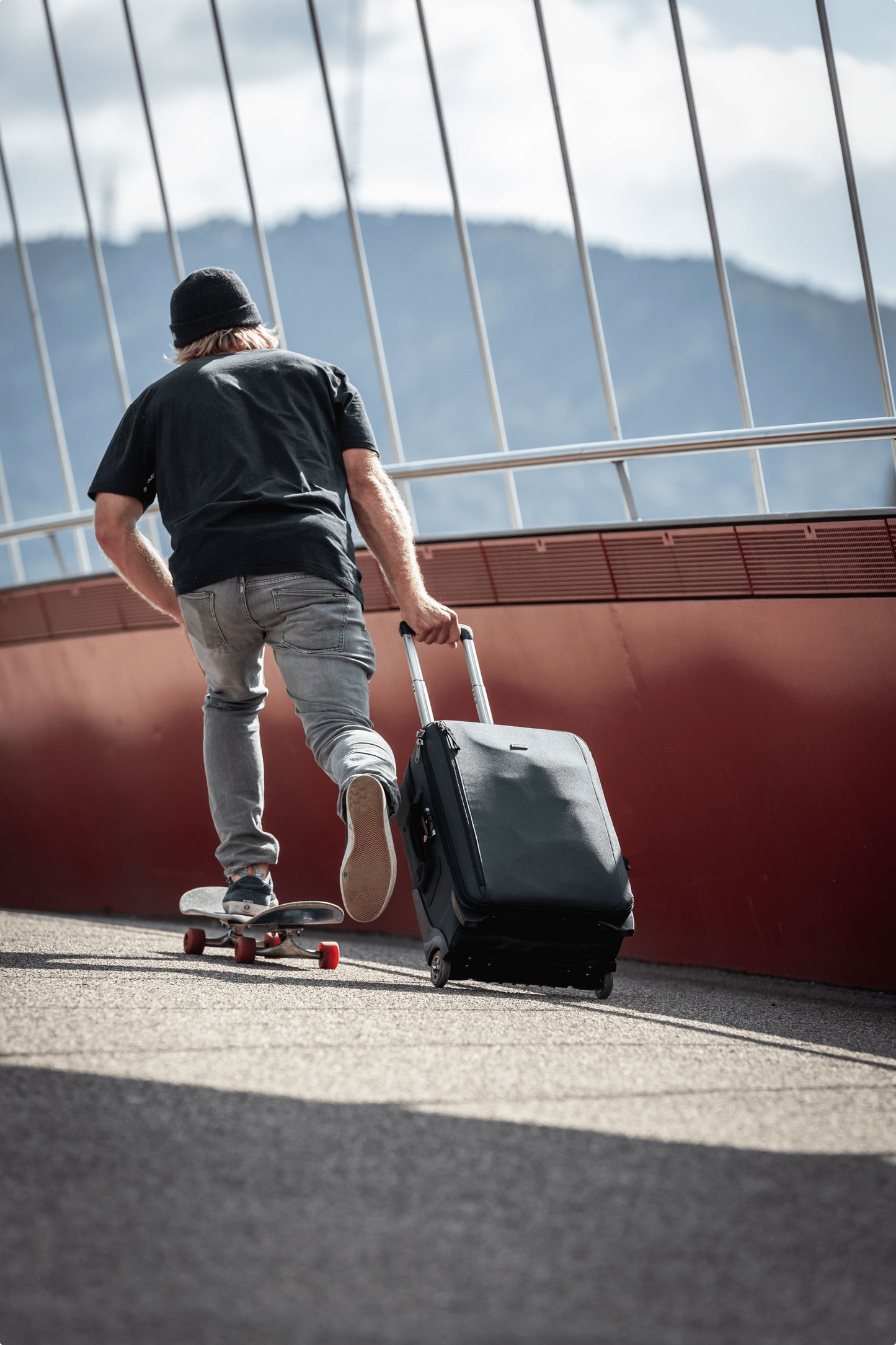 A person riding a skateboard, while rolling a suitcase behind him