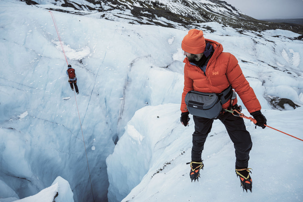 A person in the far distance climbing up a glacier, a man up close is looking back at the person in the far distance