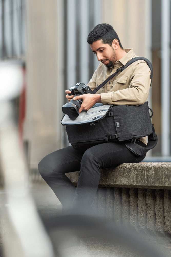 A photographer sitting on a ledge, looking through his camera propped on a small camera bag