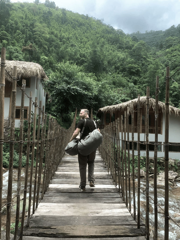 A man walking on a bridge carrying a duffle bag and is looking back 