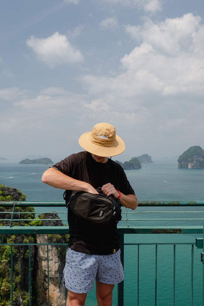 A man reaching into a black bag to grab something out, with ocean scenery background